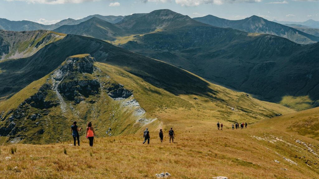 Picturesque landscape of rocky mountainous terrain covered with green grass with group of hiking travelers