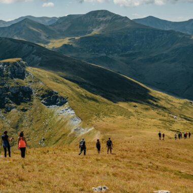 Picturesque landscape of rocky mountainous terrain covered with green grass with group of hiking travelers