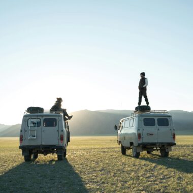 Wandering tourists standing on minibuses traveling across plain and admiring dawn over hills during vacation tour
