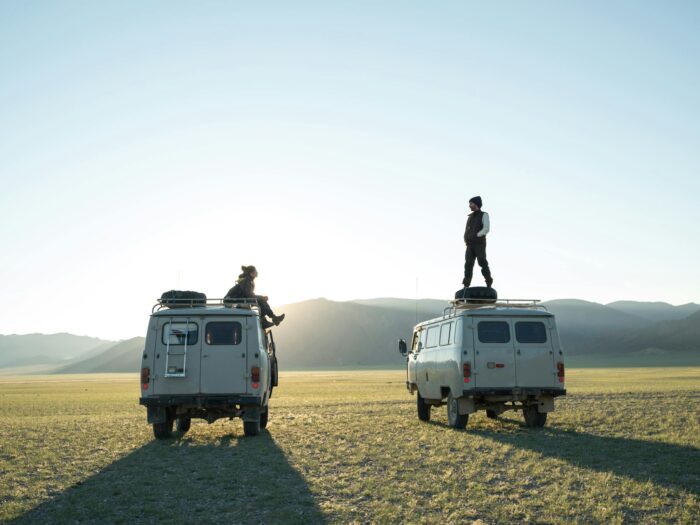 Wandering tourists standing on minibuses traveling across plain and admiring dawn over hills during vacation tour